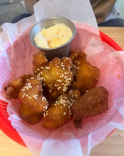 Sesame-topped hot honey chicken bites in a red basket with Kewpie mayo
