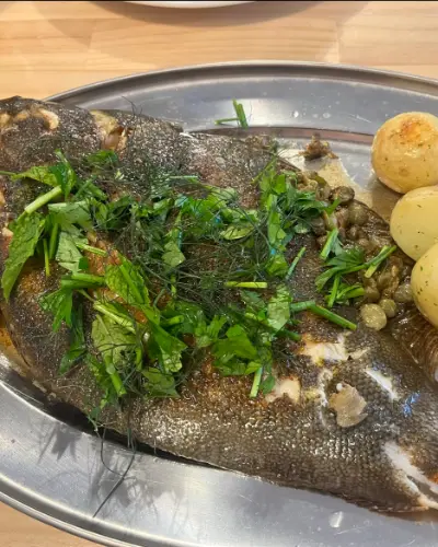 A whole grilled flatfish with herbs, capers and potatoes on a steel platter
