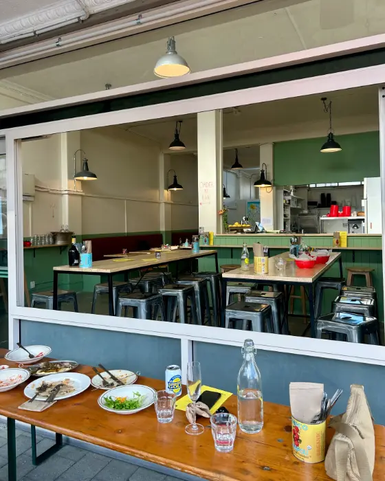 Looking through Goldie's front window: green walls, pine tables, steel stools and enamel lamps