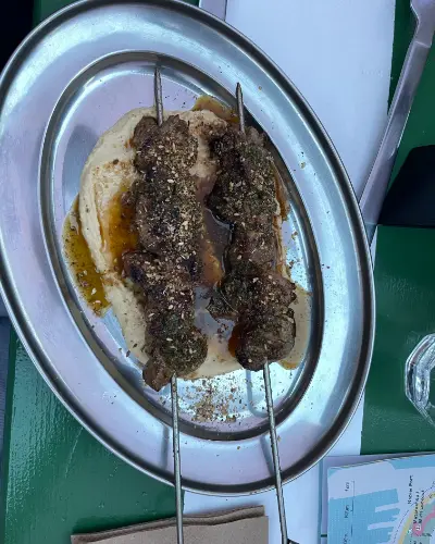 Two lamb skewers crusted with herbs and za'atar on hummus, on a steel platter